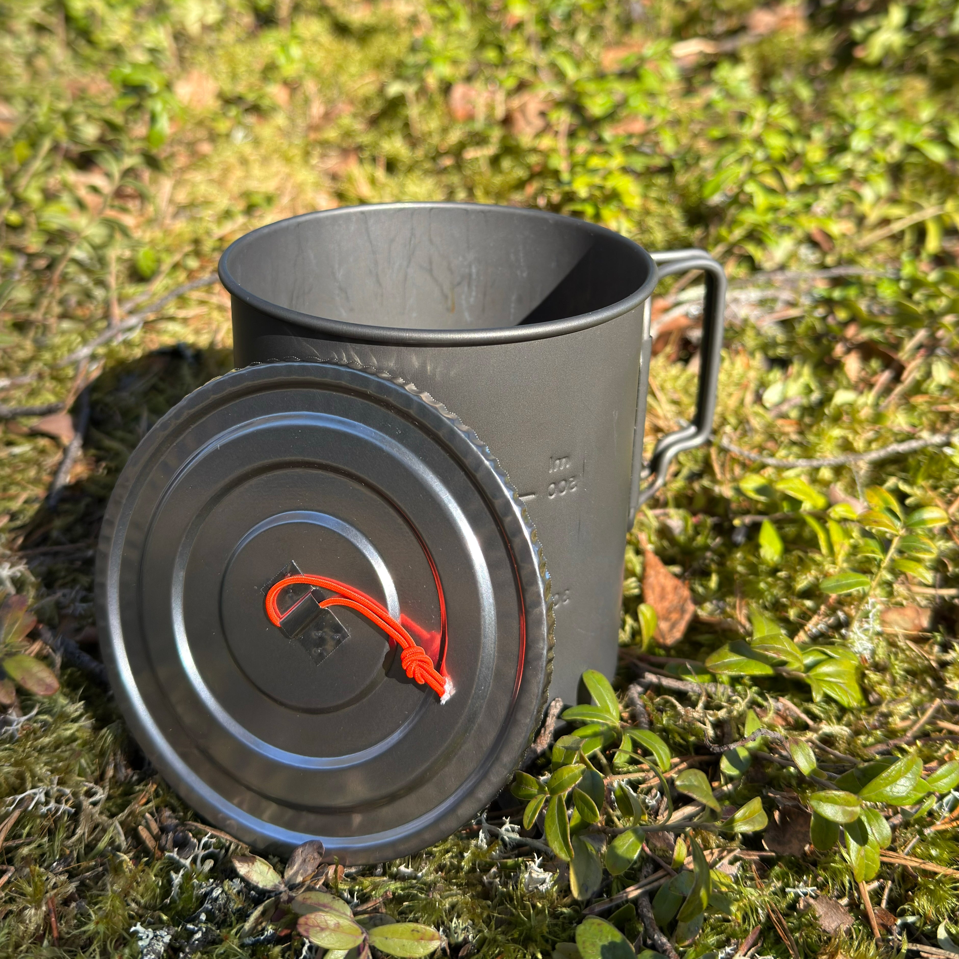 FeatherLid titanium pot lid beside a backpacking cooking pot outdoors